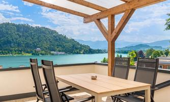 A beautiful terrace with a table and chairs. In the background, you can see a tranquil lake and green mountains.