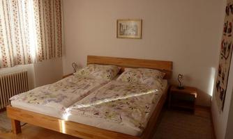A cozy bedroom with a double bed and colorful bedspreads. Curtains with a floral pattern let in plenty of daylight.