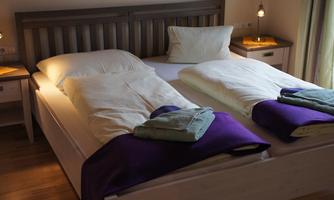 A cozy bedroom with two single beds. Each bed is adorned with white bedspreads and colorful wool blankets.