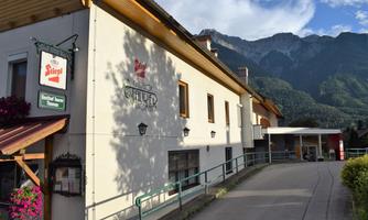 A cozy inn with an inviting entrance. In the background, majestic mountains and a blue sky can be seen.