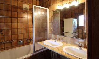 A bathroom with two sinks and a shower. The walls are tiled with brown tiles and there is a bathtub.
