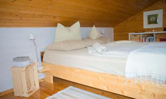 A cozy bedroom in the attic with a wooden bed frame and comfortable cushions. The warm wooden details and soft lighting create an inviting atmosphere.