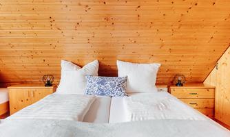 A cozy bedroom with a double bed and bright pillows. The walls are made of wood, creating a warm atmosphere.