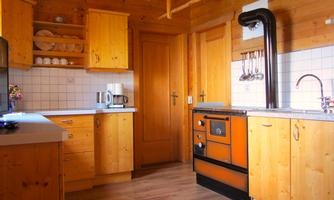 A cozy kitchen with wooden cabinets and modern appliances. The warm atmosphere is emphasized by the wooden stove and the bright walls.