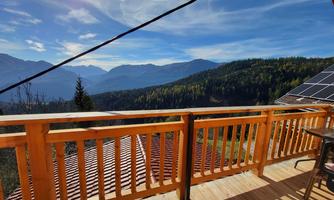 A beautiful view from a balcony of a mountainous landscape with green trees and blue mountains in the background. The sky is clear and shows some clouds.