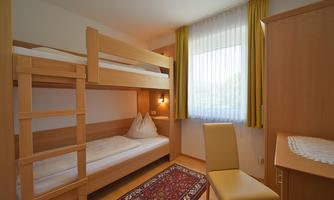 A simple room with a bunk bed and a single bed. Large windows provide plenty of daylight.