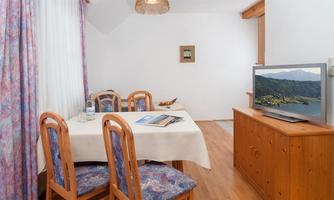 A cozy dining area with a table and wooden chairs. There is a television on the wall and a small decoration.