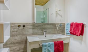 A modern bathroom with bright walls and wooden ceilings. The sink area is decorated with colorful towels.