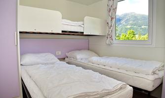 A simple room with two single beds and a loft bed. A window offers a view of the mountains.