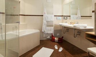 A modern bathroom with a bathtub and a shower. On the sink are towels and bathrobes.