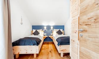 A cozy room with two single beds and wooden paneling. The walls are light blue and the lighting creates a pleasant atmosphere.