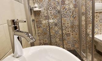 A modern bathroom with an elegant sink and colorful tiles. The shower cubicle is separated by glass walls.