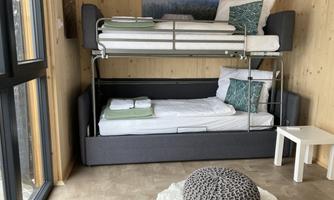 A modern room with a bunk bed and an unfolded sofa bed. There is a small table and a round rug on the floor.