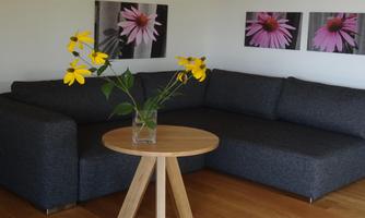 A modern living room with a gray sofa and a round wooden table. On the table, there is a vase with colorful flowers.