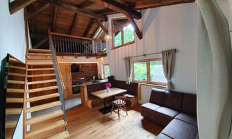 A cozy apartment in modern rustic style with a wooden staircase. The open space includes a kitchen and a seating area with a large window.