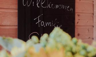 A welcome sign with the inscription "Welcome, Family" is displayed on the wall. In the foreground, sunflowers and other flowers are visible.