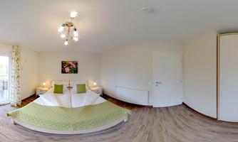 A bright bedroom with a double bed and green bedding. The walls are painted in neutral colors, and there is a nice view outside.