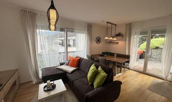 A modern kitchen-living room with a cozy sofa and a dining table. Large windows let in plenty of light and offer a view of a terrace.
