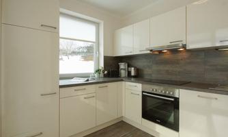 A modern kitchen with white cabinets and a black stove. It has a window that lets in a lot of natural light.
