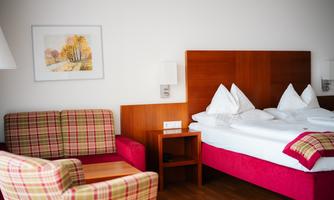 A modern hotel room with a large bed and two pillows. There is a cozy seating area with checked furniture and a picture on the wall.