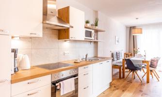A modern kitchen with white furniture and wooden countertops. In the background, there is a cozy dining area with a table and chairs.