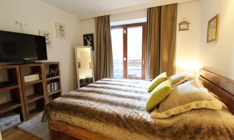 A cozy bedroom with a large bed and soft pillows. The room has bright walls, a TV, and a balcony with a view outside.
