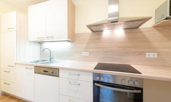 A modern kitchen with bright furniture and wooden surfaces. It includes a sink, a stove, and a range hood.