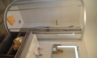 A modern bathroom with a shower cabin and a sink. The walls are light tiled and there are some towels and plants for decoration.