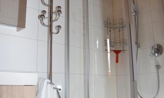 A modern bathroom with a shower and wooden ceiling. A chair setup and a towel holder are also visible.