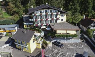A quiet hotel with several floors and a balcony, surrounded by trees and a parking area. The area is green and idyllic.