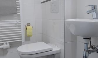 A modern bathroom with white wall tiles. On the right side, there is a toilet and a sink.