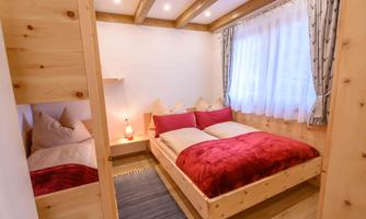 A cozy bedroom with wooden accents and warm colors. There is a double bed with red pillows and a second sleeping option.