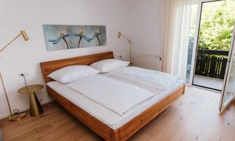 A bright bedroom with a large double bed and a wooden floor. Simple furniture and a balcony give the room an inviting atmosphere.