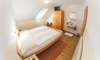 A cozy bedroom with a large double bed and wooden paneling. There is a wardrobe and a small sink in the corner.