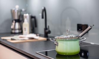 A modern kitchen area with a green pot on the stove. In the background, there is a coffee machine and other kitchen utensils visible.