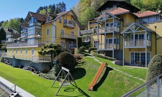 A row of beautiful, yellow houses with balconies and green lawns. In the foreground, there is a playground with a slide and a swing.