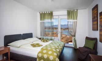 A cozy bedroom with a double bed and green bedding. Large windows offer a view of the landscape.