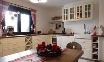 A cozy kitchen with white furniture and a wooden table. Red candles and Christmas decorations create a festive atmosphere.