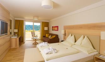 A modern hotel room with a double bed and a cozy seating area. Large windows provide a view of the landscape and plenty of daylight.