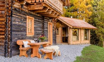 A cozy wooden house with a large balcony and a porch. Outside, there is a wooden table set in a picturesque setting.