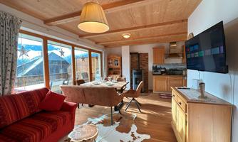 A cozy living area with a red sofa and a wooden table. Large windows provide a view of the mountains, and the Danish country house design creates a warm atmosphere.