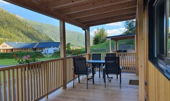 A cozy terrace with a table and chairs, surrounded by a beautiful mountain landscape. The wooden structure creates an inviting atmosphere.