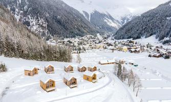 A picturesque winter landscape with snow-covered mountains and a small village in the valley. Wooden chalets are arranged in the foreground, giving the picture a cozy atmosphere.