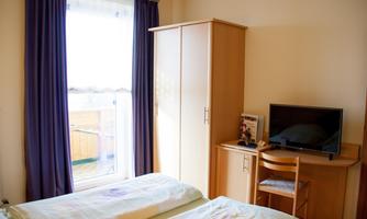 A simple room with two single beds, a desk, and a television. A window with curtains provides a view outside.