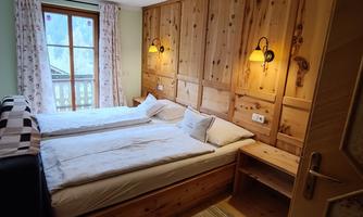 A cozy bedroom with two beds and warm wooden walls. A window offers a view outside and provides natural light.
