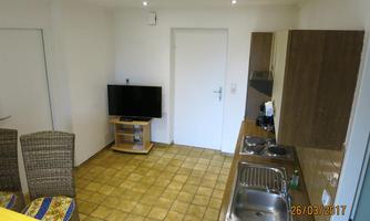 A cozy kitchen with a small seating area and a television. The walls are light, and the floor is tiled.