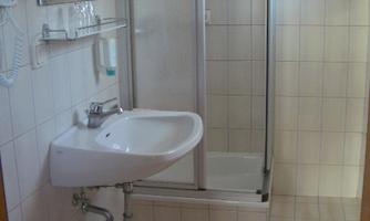 A small bathroom with a shower and a sink. Two towels in soft colors hang on the wall.