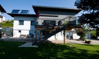A modern house with a garden and a terrace. The outdoor staircase leads to the upper floor, and the surroundings are green and inviting.