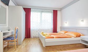 A bright and modern bedroom with two beds and a desk. Large windows with curtains let in plenty of light.
