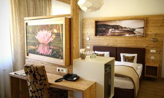 A stylish room with wood decor and a cozy bed. The room features a desk and modern artworks on the wall.